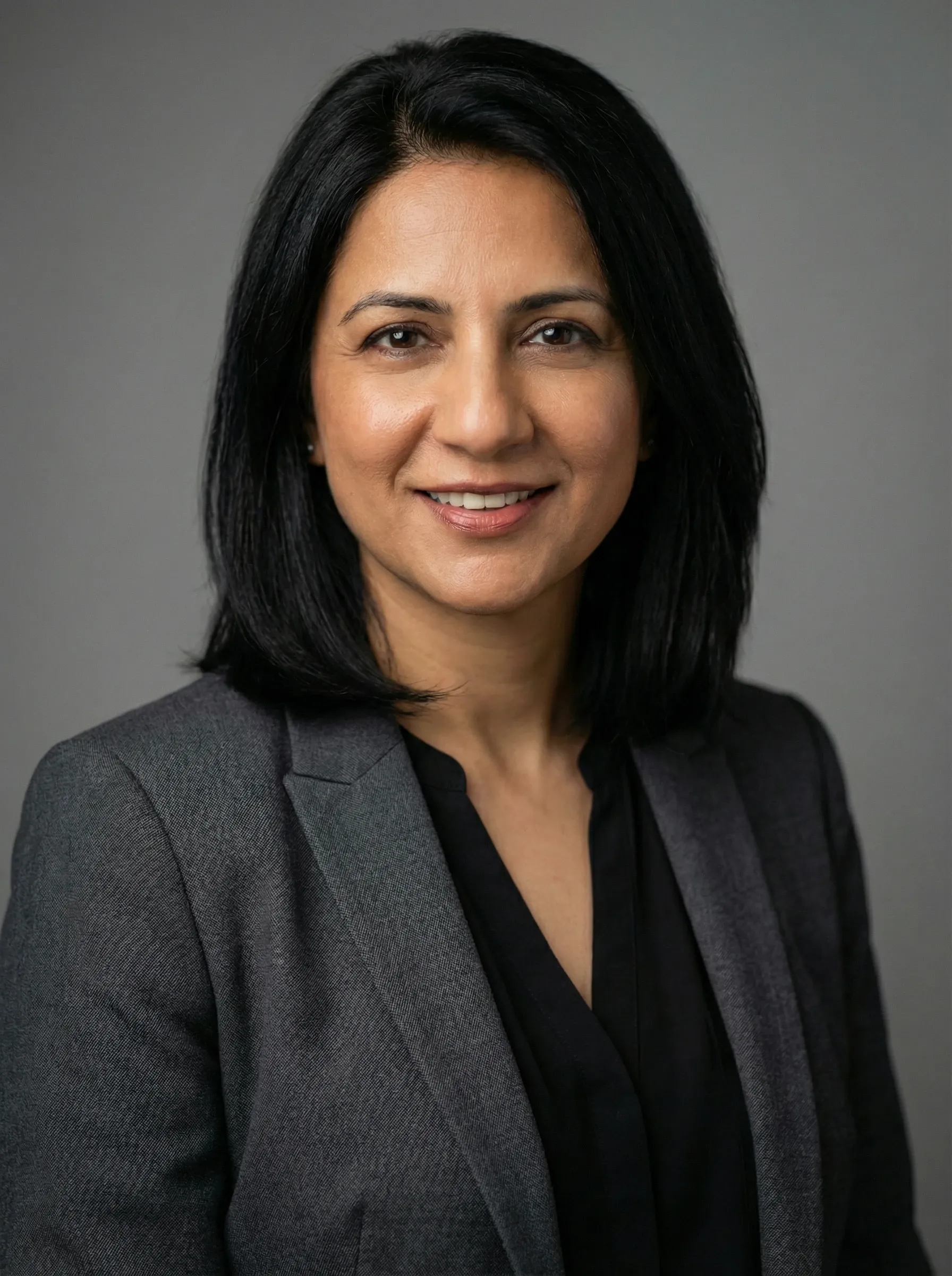 Professional headshot of a woman in a charcoal blazer and black blouse against a gray studio background